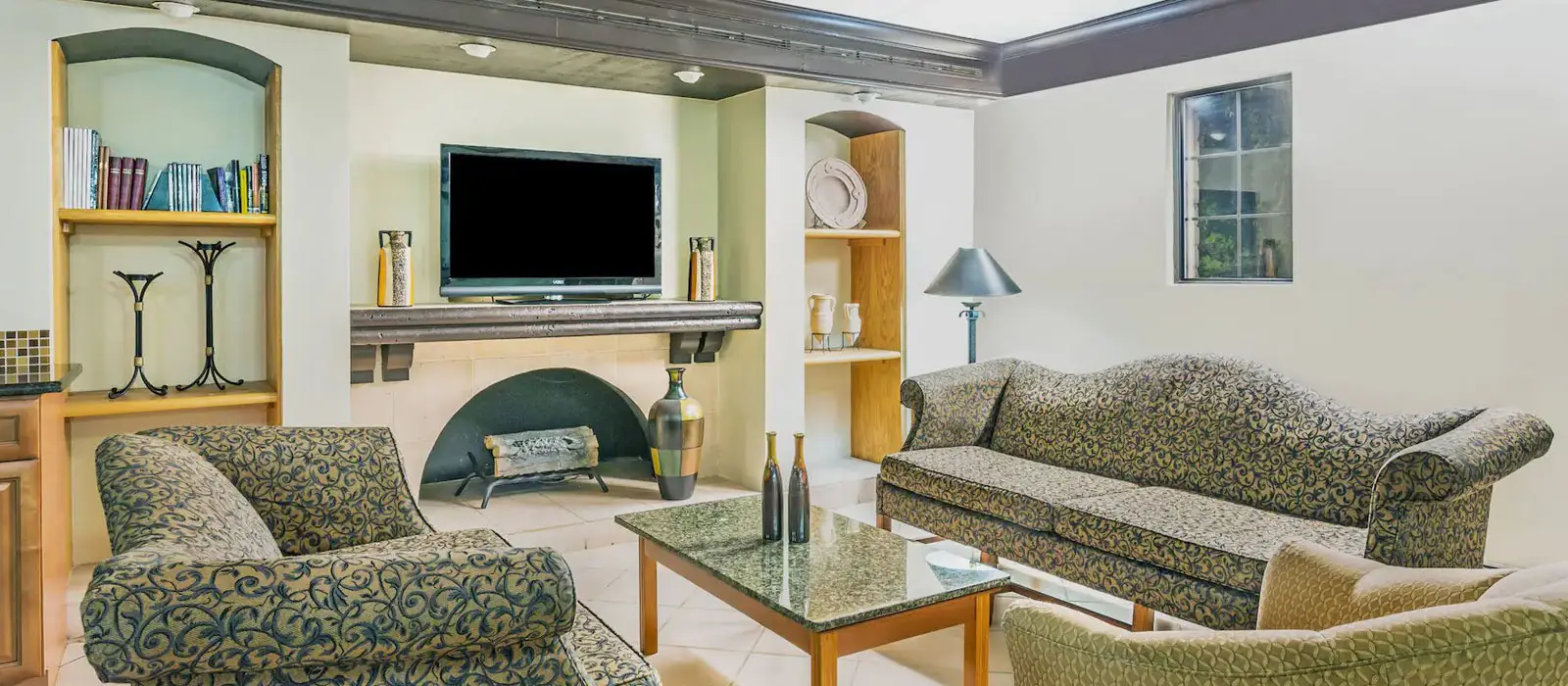 A living room with two patterned sofas, a coffee table, a fireplace, a wall-mounted TV and built-in shelving