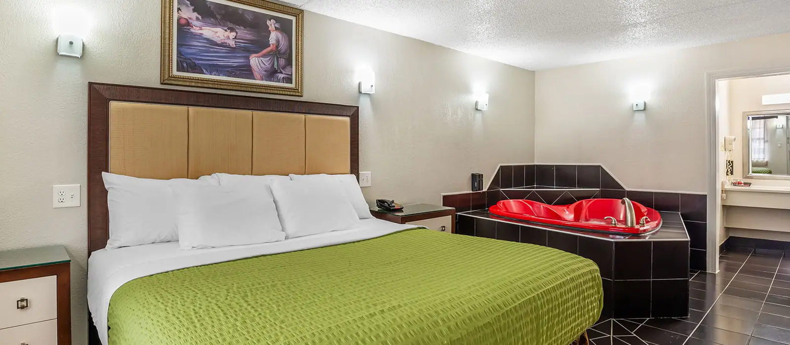 A guest room with a bed with a green blanket, a red heart-shaped hot tub and a bathroom entrance