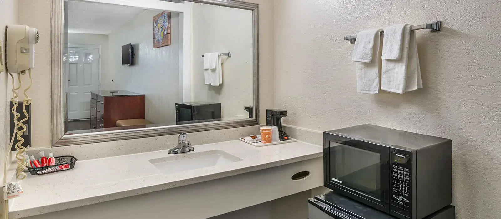 A bathroom vanity with a sink, a mirror reflecting the room, a hairdryer, a coffee maker and a microwave