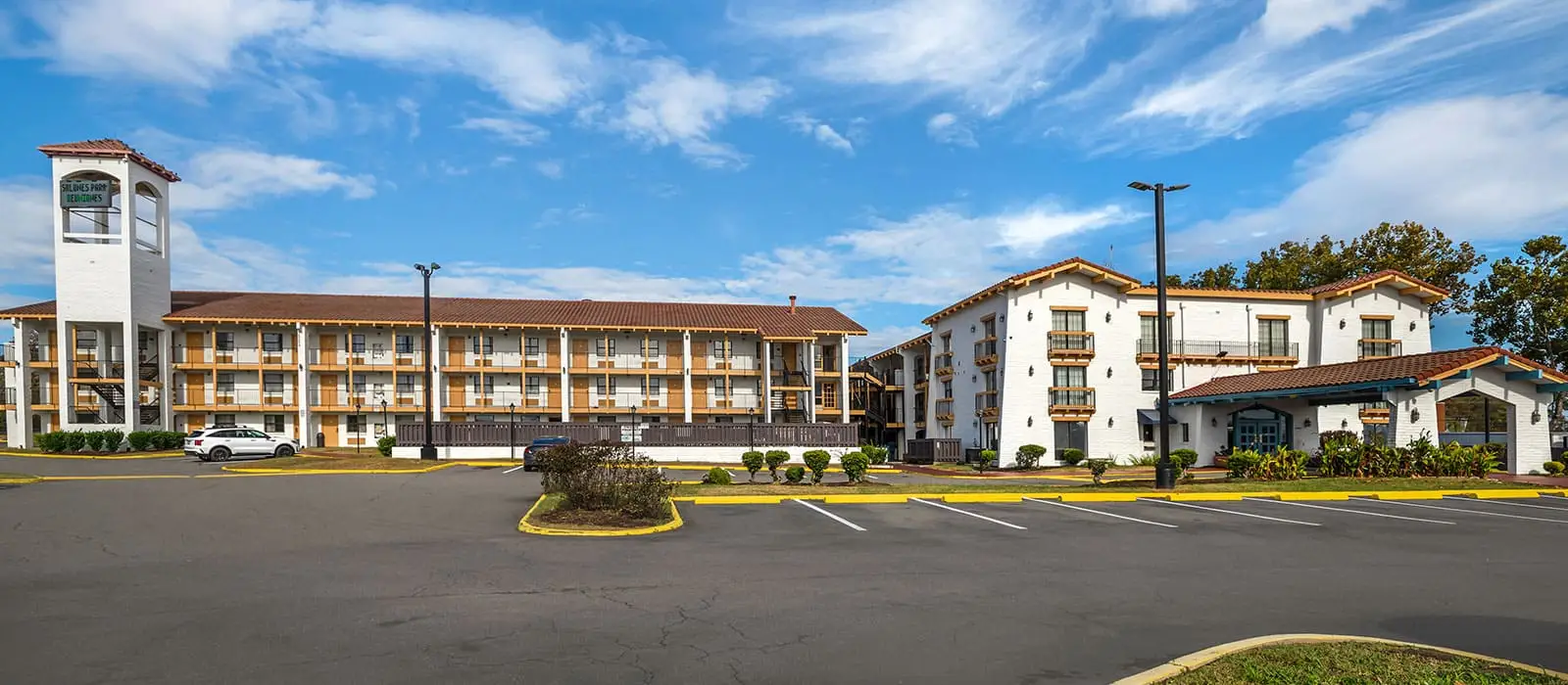 Two white buildings with brown tiled roofs and balconies, one with a tower displaying a sign that reads "SALINAS PARK RESIDENCES", are visible from a car park