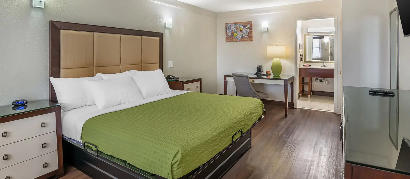 A hotel room with a bed, a desk with a chair, a television and an open doorway to a bathroom
