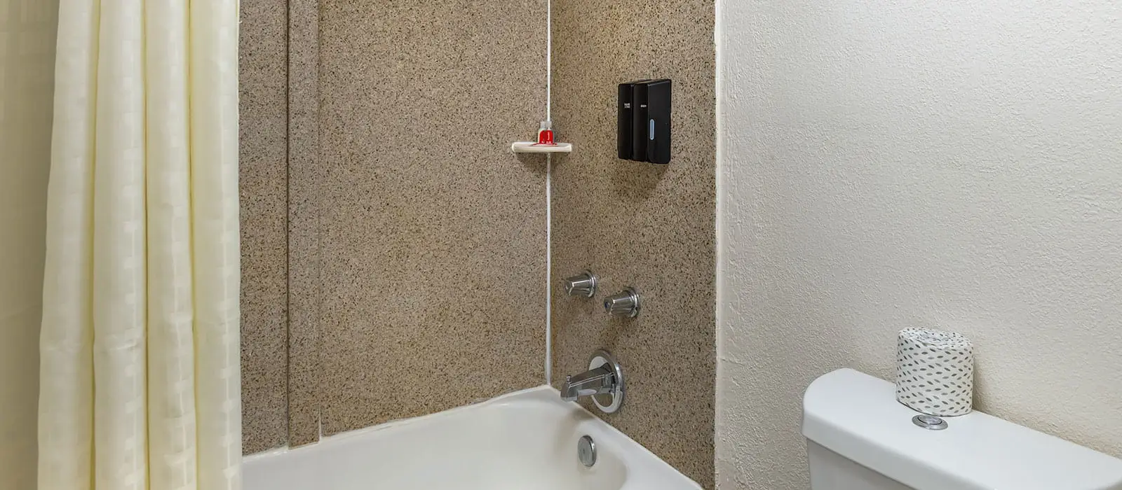 A bathroom with a white bathtub, a shower curtain, and a toilet with a roll of toilet paper on top