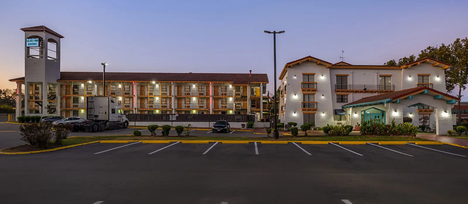 Two multi-storey buildings with red tiled roofs and white walls, a parking lot with cars and a truck, and a sign that reads "CHILDREN'S PARK RESIDENCES" on the left