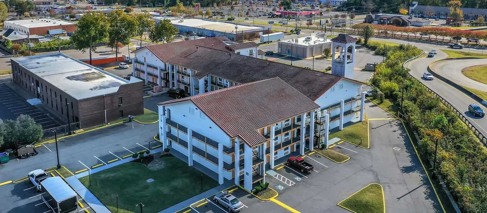An aerial view of a hotel with terracotta roofs and white walls, a neighbouring flat-roofed building and a winding road with cars
