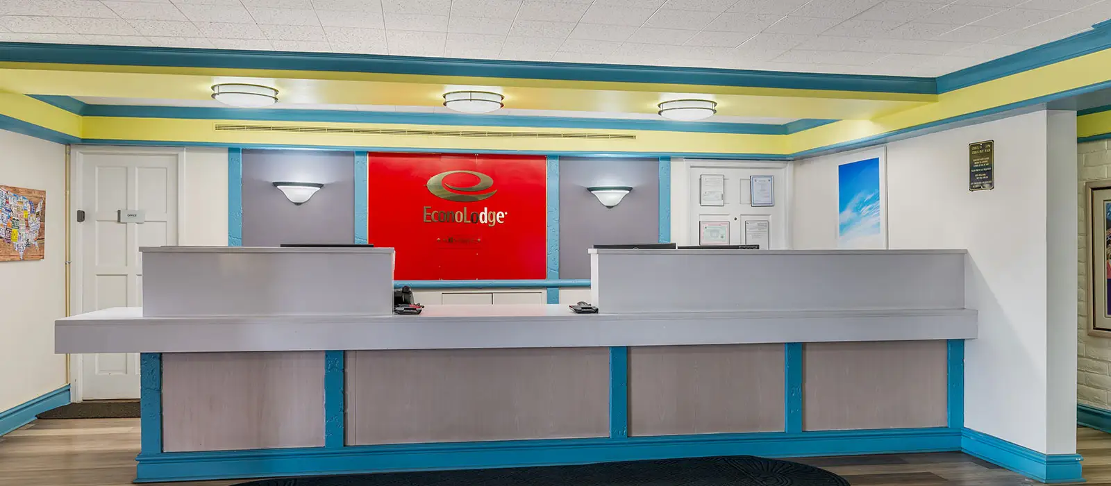 A hotel reception area with two grey counters, a red wall with the "EconoLodge" logo and light blue trim