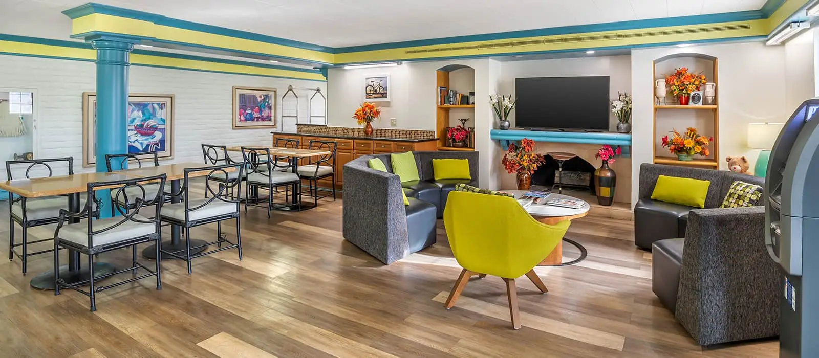 A common area with several tables and chairs, a counter with bar stools, a sofa seating area, and a television above a fireplace