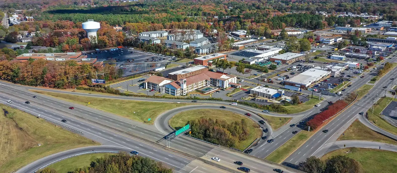 An aerial view of a multi-lane highway interchange with surrounding buildings and autumn trees