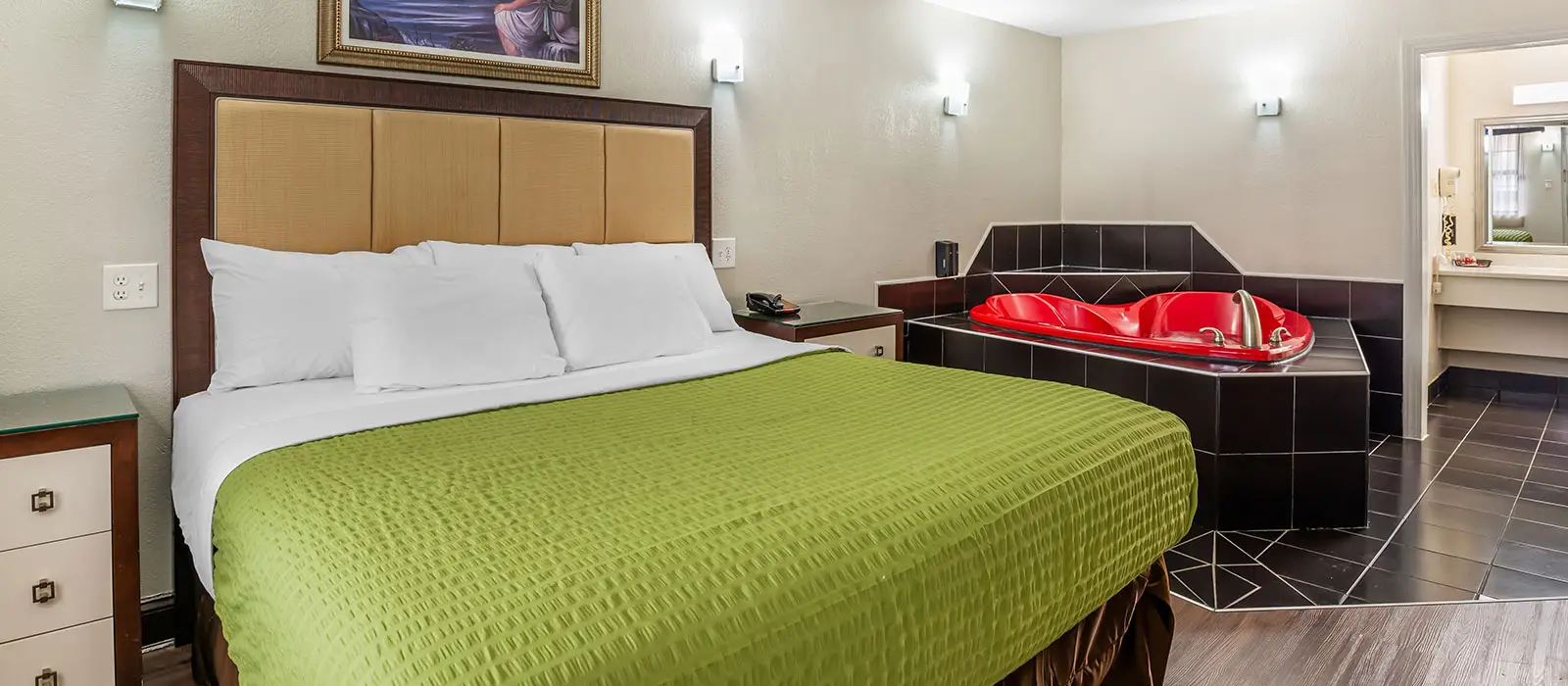 A guest room with a bed with a green bedspread, a red hot tub, and a partial view of a bathroom
