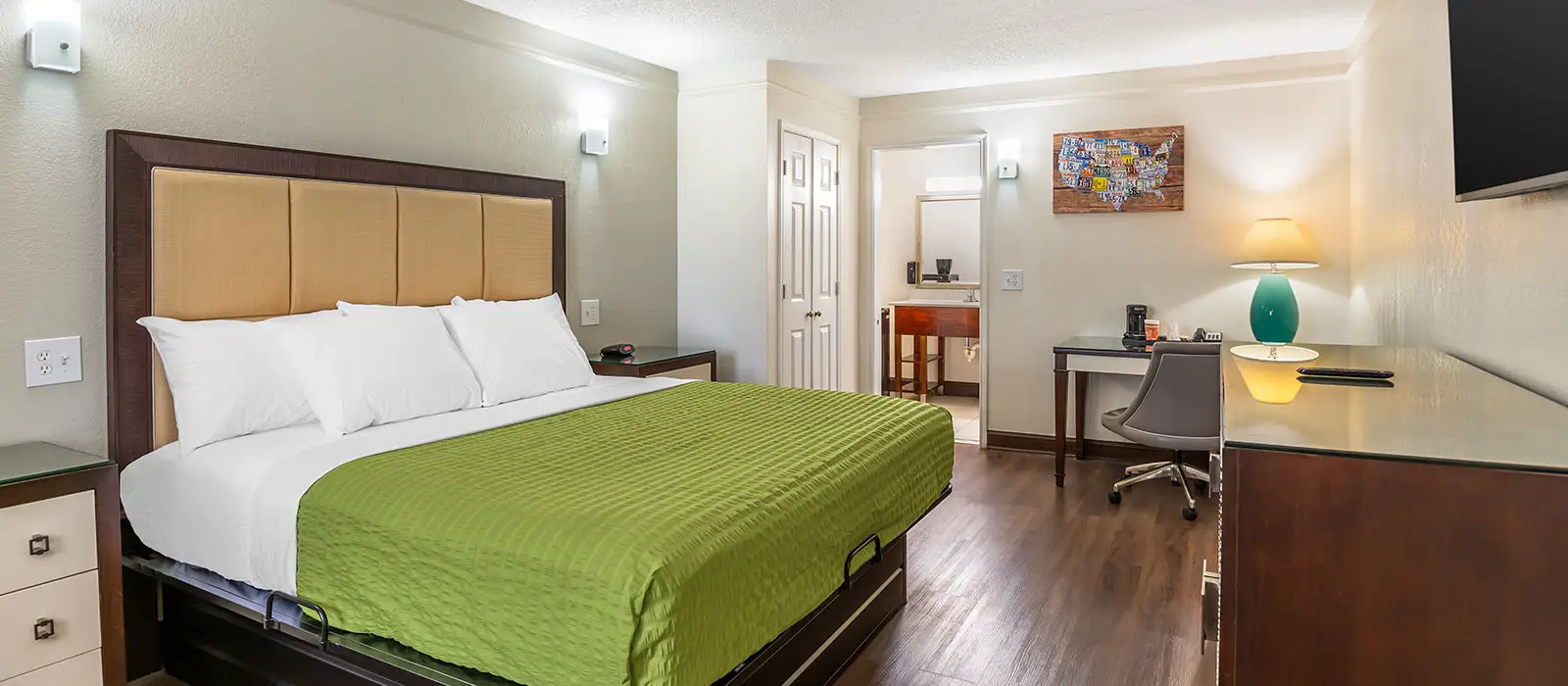 A guest room with a bed, a desk and chair, a television, and a partial view of a bathroom