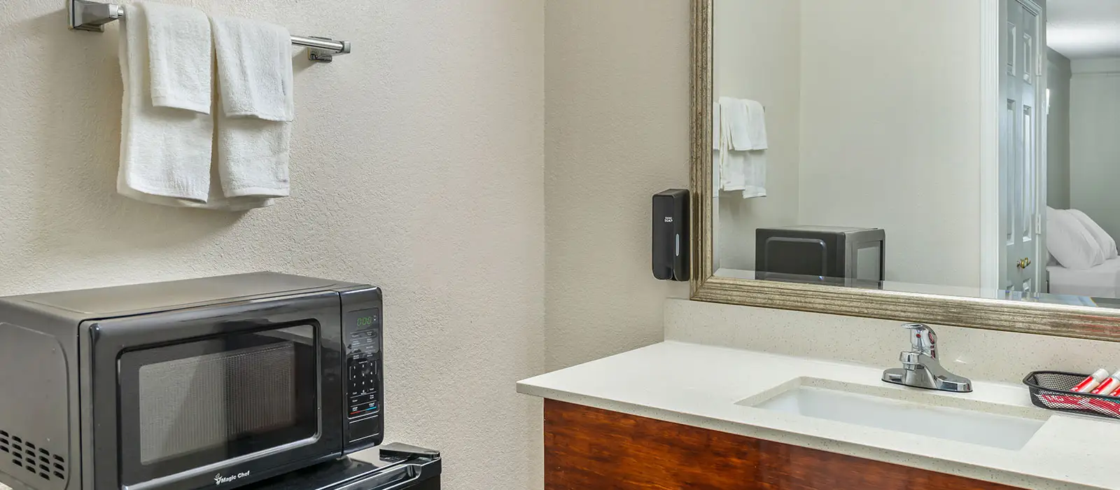 A microwave sits on a black counter next to a bathroom vanity with a sink and mirror