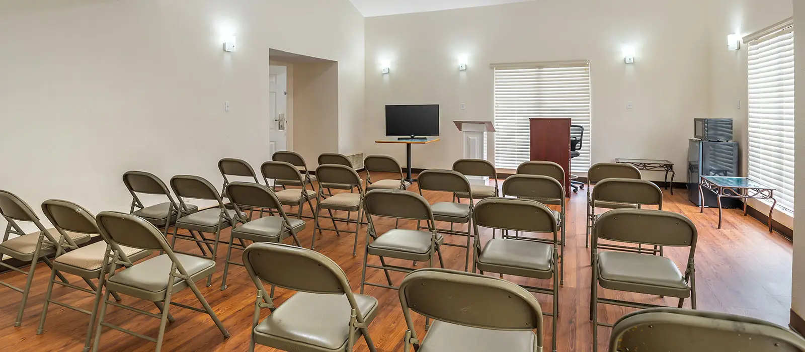 A conference room with rows of grey folding chairs facing a screen, a podium and a lectern