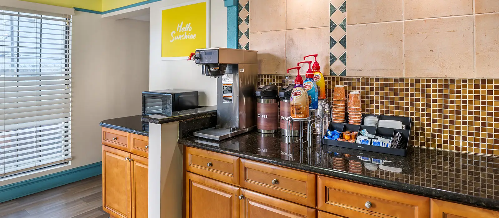 A coffee station with a coffee maker, microwave, coffee carafes, creamers, cups and a variety of condiments