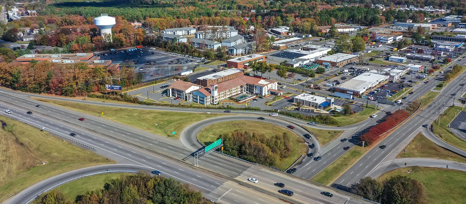 An aerial view of a multi-lane highway interchange with cars travelling, surrounded by buildings and autumn trees