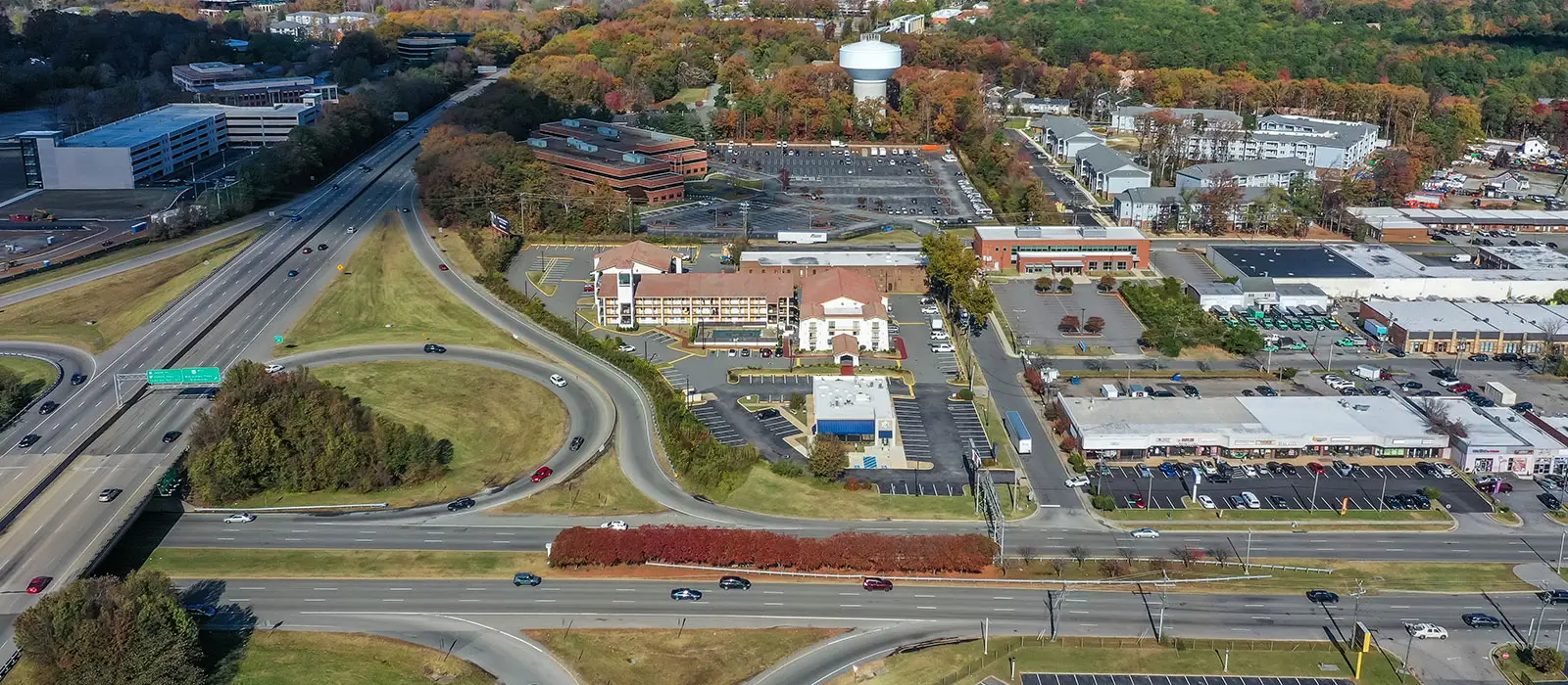 An aerial view of a highway interchange with cars travelling, surrounded by buildings and trees with autumn foliage
