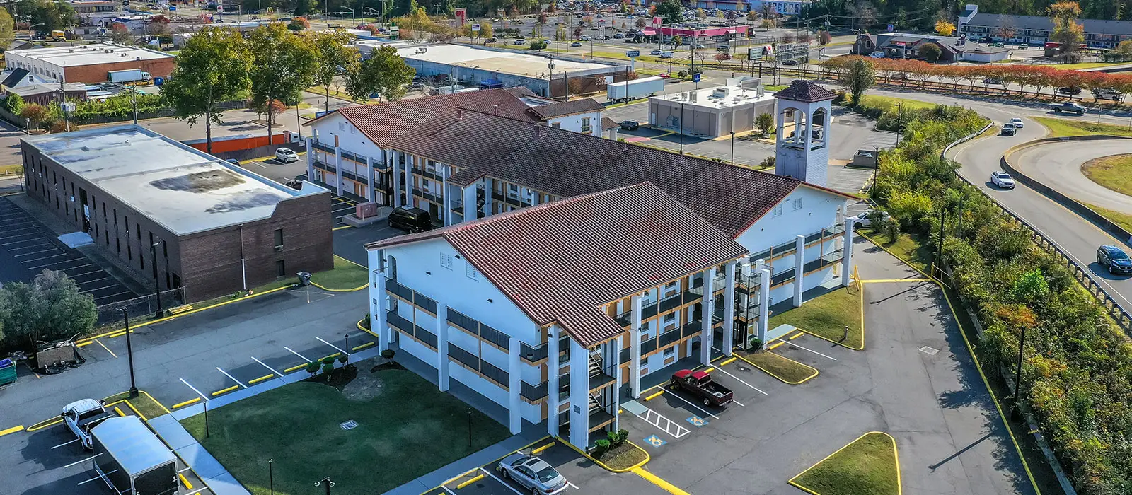 An aerial view of a hotel complex with multiple buildings, parking lots, and a winding road with cars